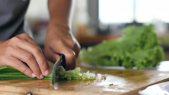 Close Up of Scallion Being Chopped on a Wooden Chopping Board By a Woman's Hand.