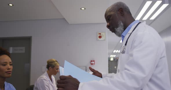 Diverse male doctor at hospital reception and talking to female staff