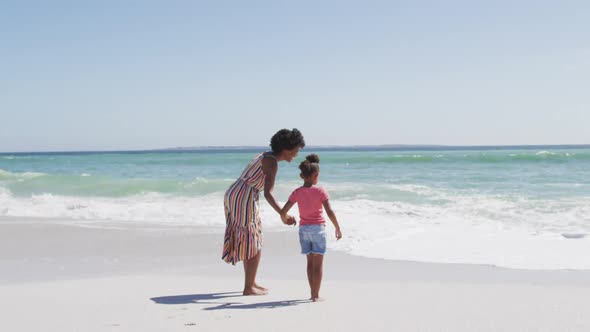 Smiling african american mother with daughter walking on sunny beach