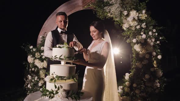 Newlyweds Cut the Wedding Cake Lovely Bride and Groom Couple Cutting Dessert with a Knife Outdoors