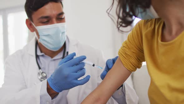 Hispanic male doctor making injection to girl at home, all wearing face masks,