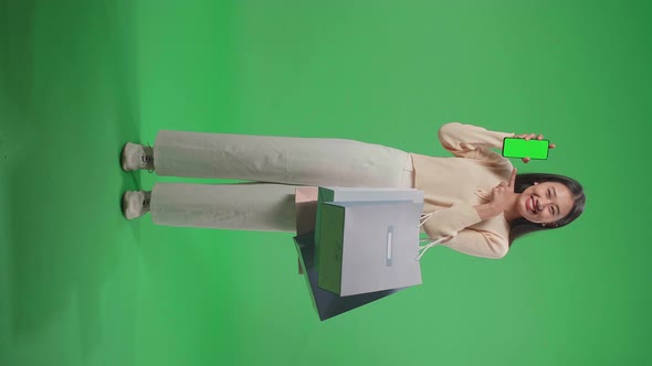 Asian Woman With Shopping Bags Holding And Pointing Green Screen Mobile Phone On Green Screen