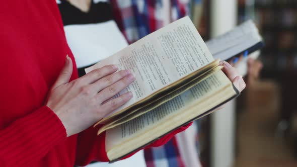 Close-up of white female hands turning the page of a book, against the background students, closeup.