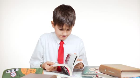 Young Caucasian School Kid Sorting Out Books Sitting at Table and Folding Pages on White Background