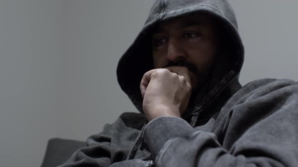 An Indian man wearing a hoodie with a clutched hand covering his face, the man in a dark psychologic