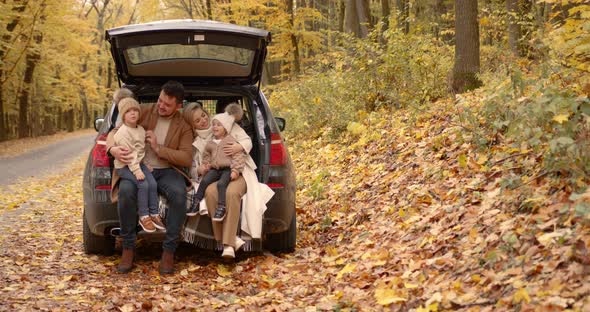 Happy Family Sitting in the Trunk in the Autumn Park