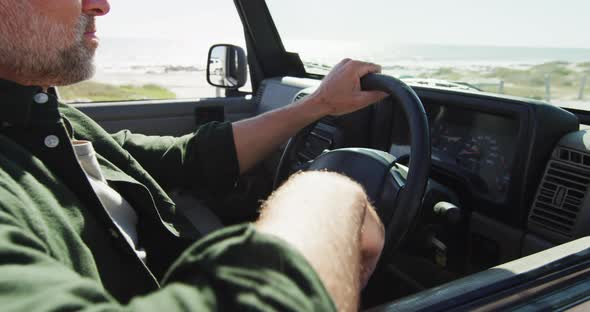 Caucasian man sitting in car admiring the view on sunny day at the beach