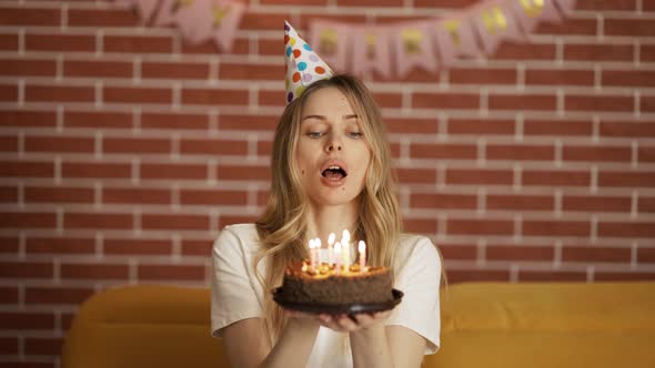 Portrait of Pretty Girl Holding Birthday Cake and Blowing Candles at Party