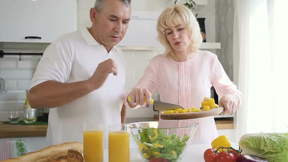 Senior Man Helping Mature Wife Putting Cut Pepper To Salad Bowl