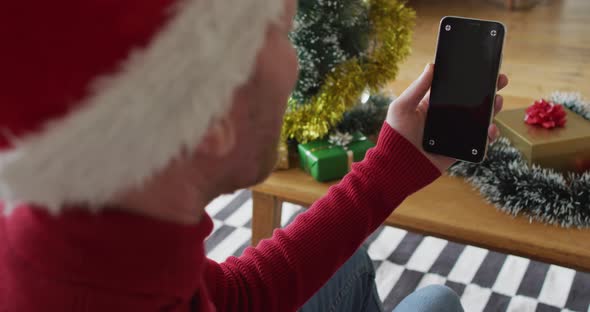 Happy albino african american man wearing santa hat using smartphone at christmas