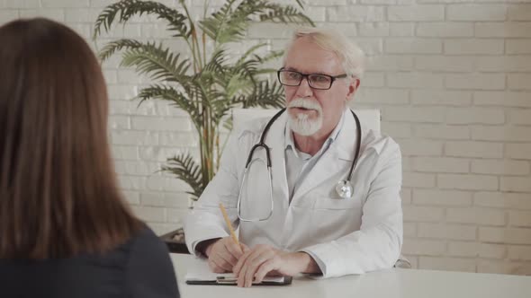 Elderly Doctor Consults a Woman Patient in a Clinic