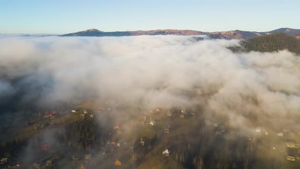 Aerial View of Vibrant Landscape of Foggy Clouds Covering Mountain Hills and Small Scattered Village