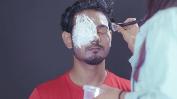 Make up artist coloring mask with brush on man's face for Halloween night