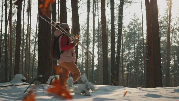 A Young Woman Carrying Skis on Her Shoulder Walks Through the Forest