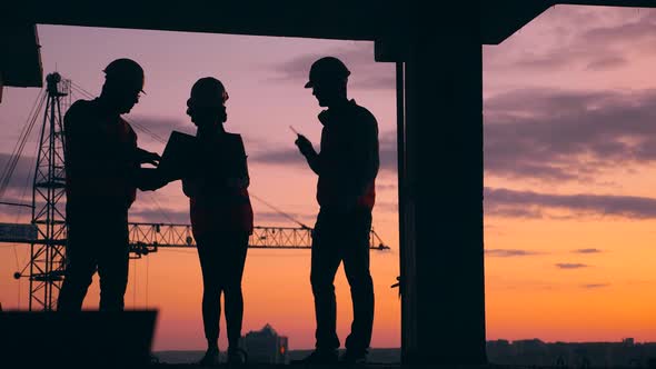 Three Engineers Work on a Construction Site on a Sunset Background. Construction Workers at Modern