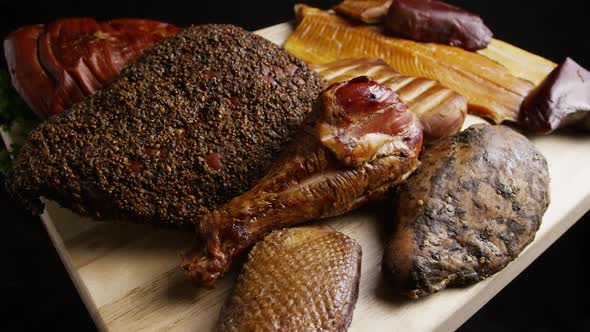 Rotating shot of a variety of delicious, premium smoked meats on a wooden cutting board