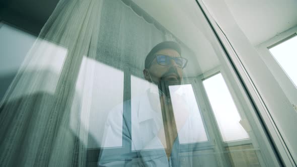 A Man Is Putting on a Medical Mask While Looking Through the Window During Pandemic of Coronavirus