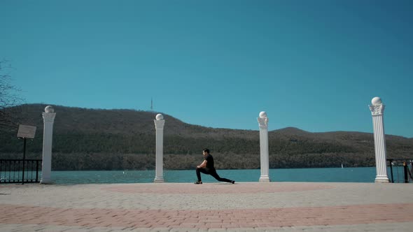 Man in sportswear does stretching and warming up in a beautiful place on the lake 