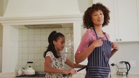 African american girl tying apron on her mother in the kitchen at home