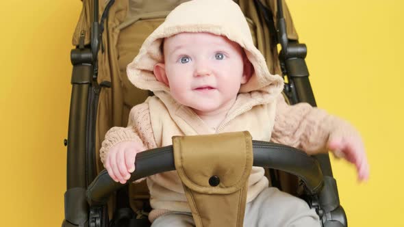 A happy child is sitting in a baby carriage on a studio yellow background. Smiling toddler baby boy