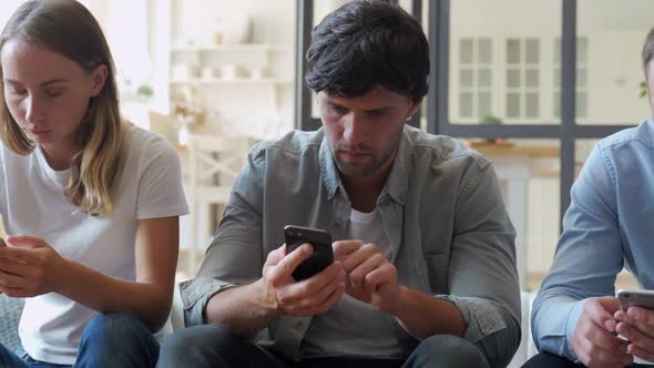 Group of Three Friends Hanging Out but Ignoring Each Other While Using Their Smartphones at Home