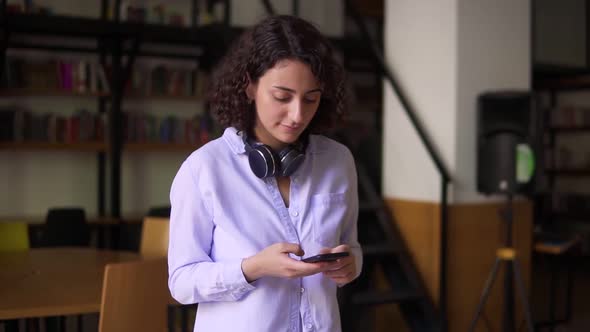 Portrait of Walking Brunette Woman Wearing White Blouse Looking on Smartphone Screen in Her Hands