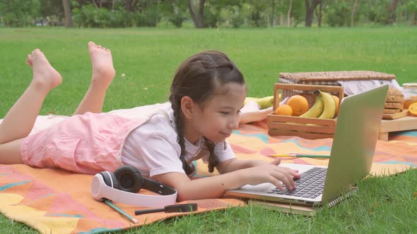 Happy little girl child smiling, learning and having fun looking at laptop computer in summer park