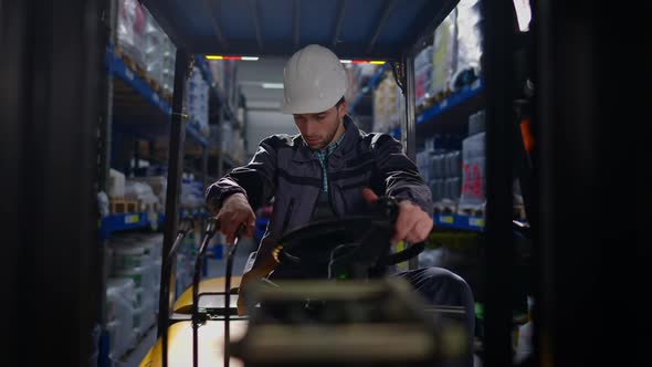 Portrait of Concentrated Caucasian Young Man in Hard Hat Turning on Forklift Sitting in Vehicle