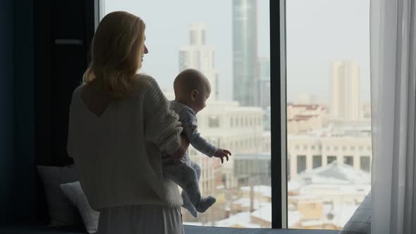 mother with baby in her arms looking out the window at the city