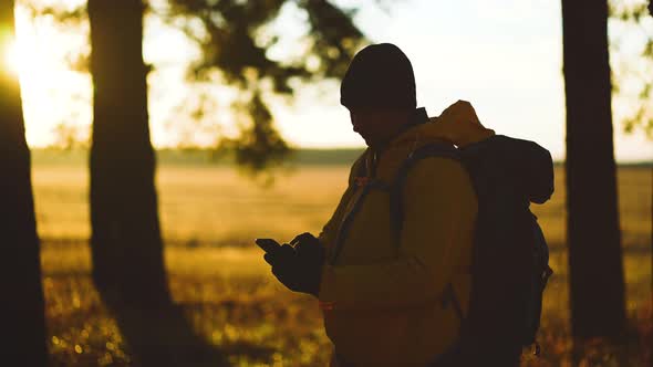 Man Hiker Backpacker Traveler Camper with Her Phone Looks at a Map or Route Under Sun Light