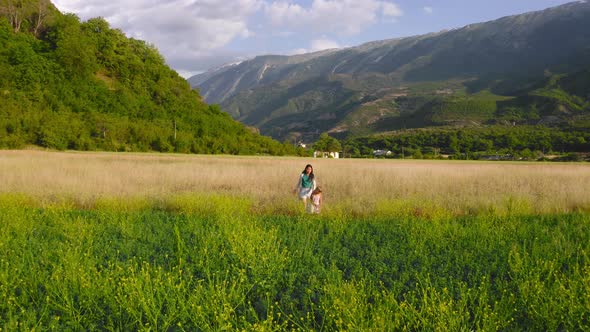 mother and daughter stroll along beautiful flowering field in Permet valley, Albania.