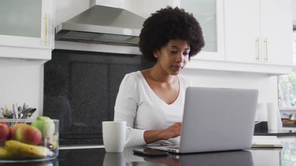 African american woman using laptop in the kitchen while working from home