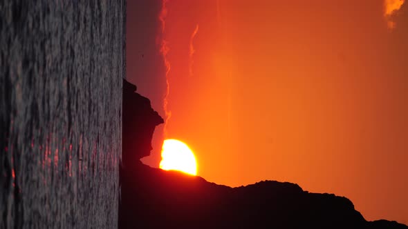 A Red Burning Sunset Over the Sea with Rocky Volcanic Cliff