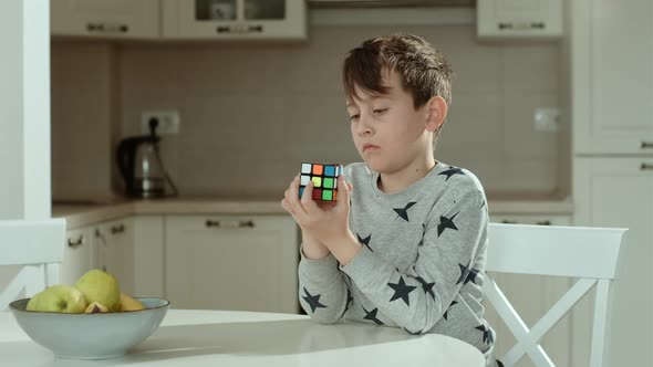 Concentrated boy in grey sweatshirt holding cube and playing with it. 