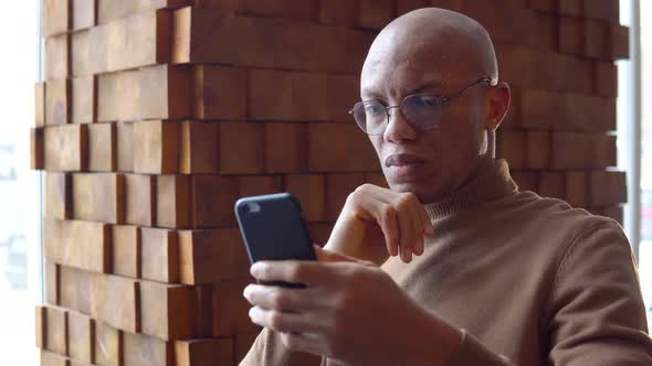 Serious Young African Man Working in a Cafe Using a Smartphone