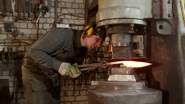 A Man Blacksmith Forming a Knife Using an Industrial Pressure Machine in Workshop