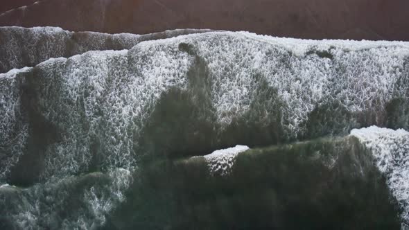 Overhead drone shot of waves crashing onto a beach on the Oregon coast during sunset. This relaxing