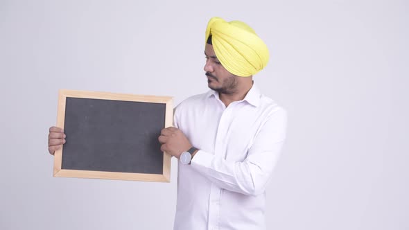 Stressed Bearded Indian Sikh Businessman Holding Blackboard and Giving Thumbs Down