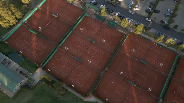 Aerial high angle view revealing tennis courts between a golf course and a parking lot on a sport cl