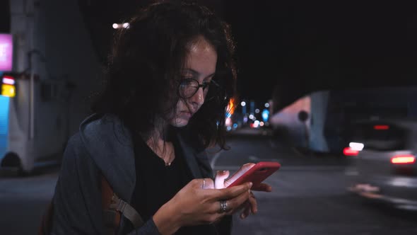 Attractive Woman Using Mobile Phone During Walk on Streets of Night Town