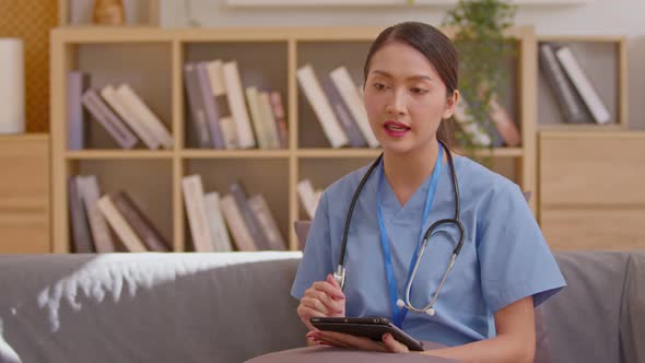 Asian doctor in blue medical uniform with stethoscope talk to the patient through the camera, lookin