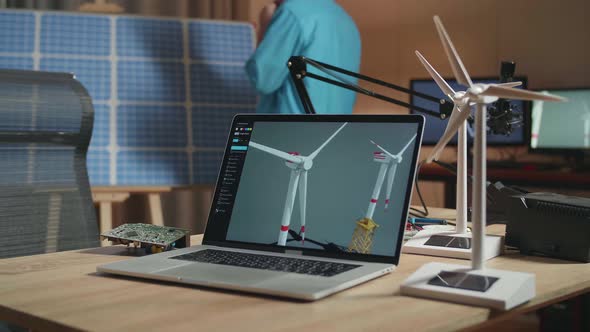 Laptop Showing Wind Turbine On The Table While A Man Walks Into The Office To Look At Solar Cell