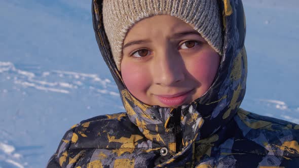 A Boy with Ruddy Cheeks in the Background of the White Snow Smiles at the Viewer