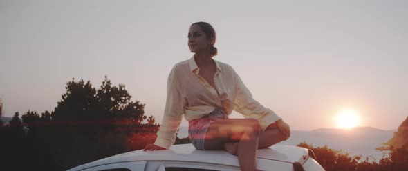 A girl sitting on the roof of her car admiring the surrounding landscape