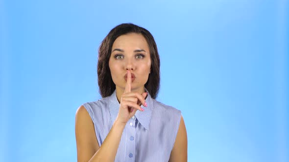 Pretty Young Woman Is Telling a Secret with Her Finger on the Mouth