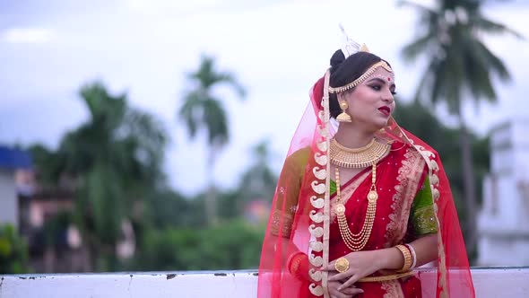 Smiling Indian Bengali bride walks on roof under cloudy dark sky at sunset