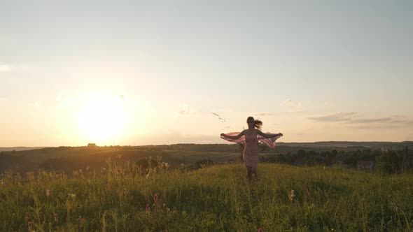 Back view of happy young woman running with USA national flag outdoors at sunset. Positive girl 