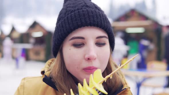 Beautiful Blonde Eats Potato Chips Against Background of Winter Market