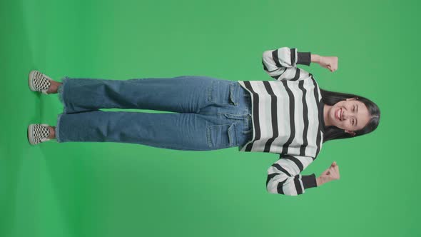 Full Body Of A Smiling Asian Woman Flex Muscle While Standing In Front Of Green Screen Background