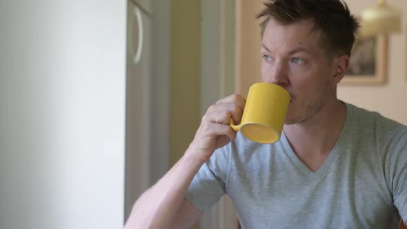 Thoughtful Young Man Drinking Coffee While Looking Through The Window